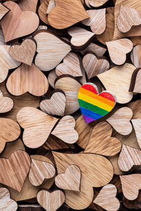 Painted wooden heart like a LGBT pride rainbow flag on wooden heart background. Greeting card.